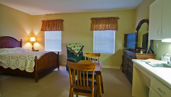 A cozy bedroom with a small dining area, featuring a wooden bed, dining table with chairs, and a television.