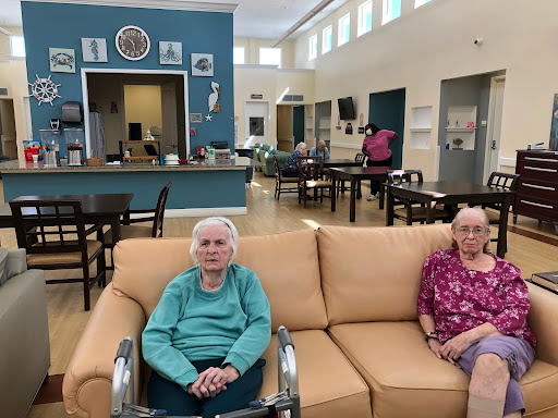 Two elderly women comfortably seated on a couch in a spacious common area of a residential facility.