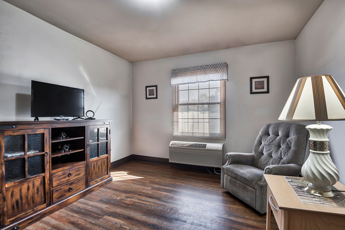 A cozy living room with wooden floors, a television, and an armchair by the window.