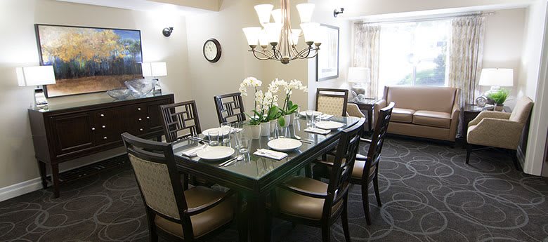 A formal dining room featuring a dark wood table set for dinner, with elegant chairs and a centerpiece of white orchids under a chandelier.