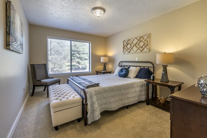 A cozy bedroom with a double bed, bedside tables, and lamps, featuring a large window and neutral decor.