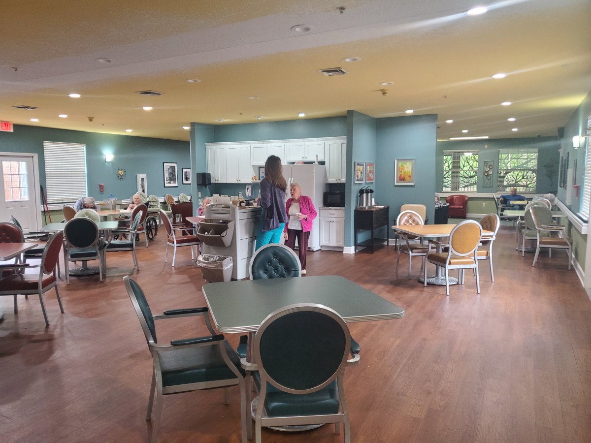 A modern cafe with tables and chairs, where people are interacting near the counter.