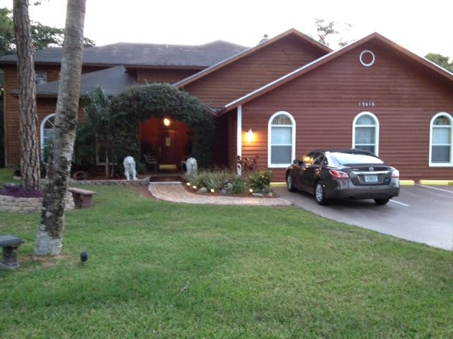A suburban house with a neatly maintained lawn and garden, featuring a car parked in the driveway during the evening.