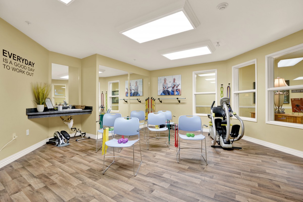 A well-lit exercise room with chairs, fitness equipment, and mirrors.