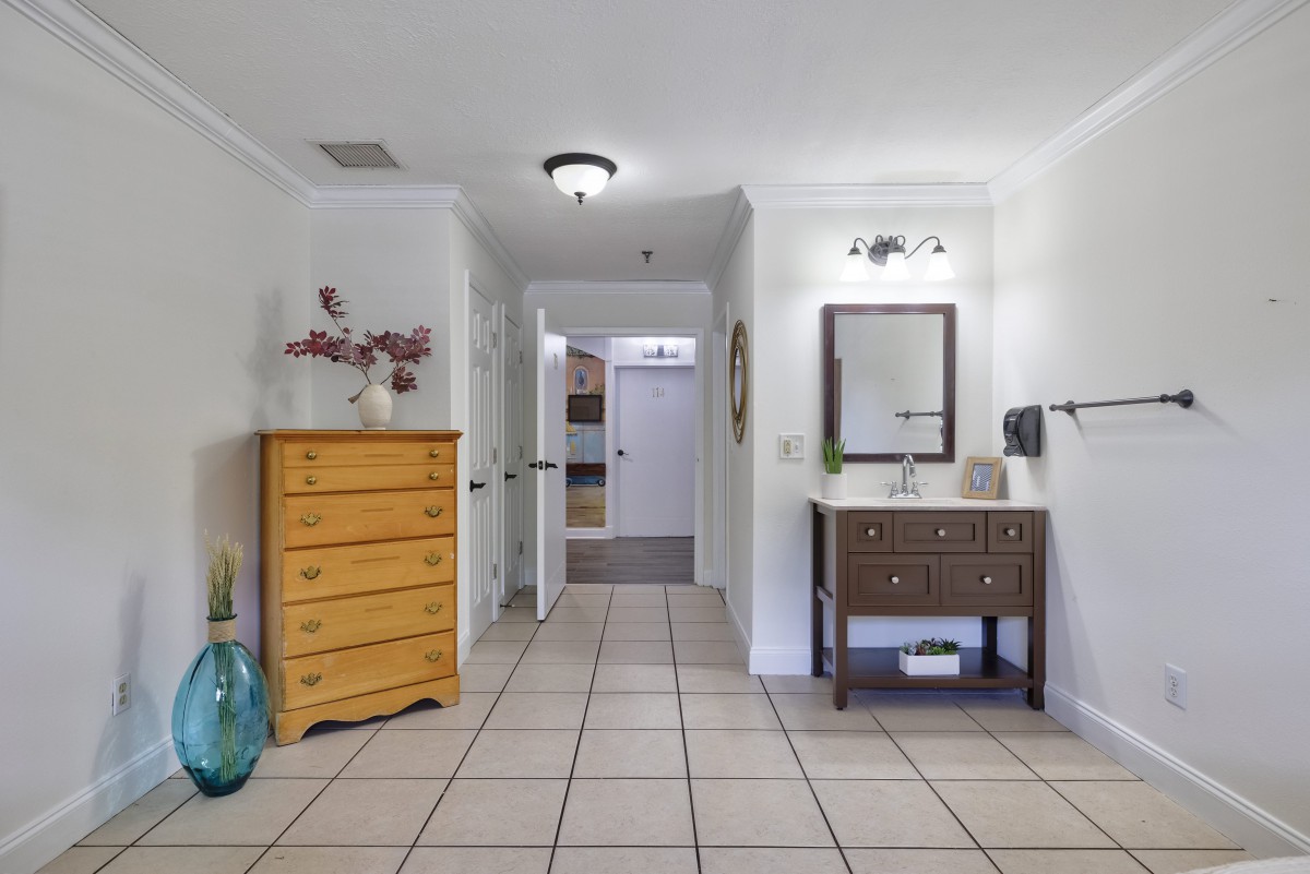 A hallway with a dresser on the left and a sink with a mirror on the right, featuring tile flooring.