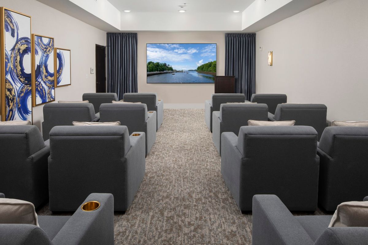 A modern home theater room with rows of comfortable gray seating, a large screen, and elegant decor.