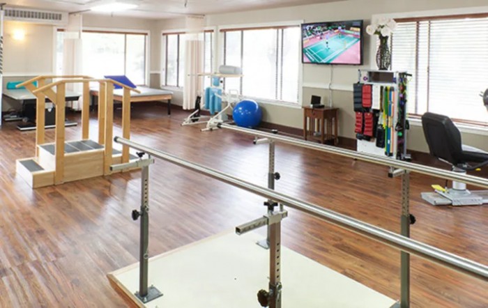 A physical therapy room equipped with parallel bars and various exercise equipment.