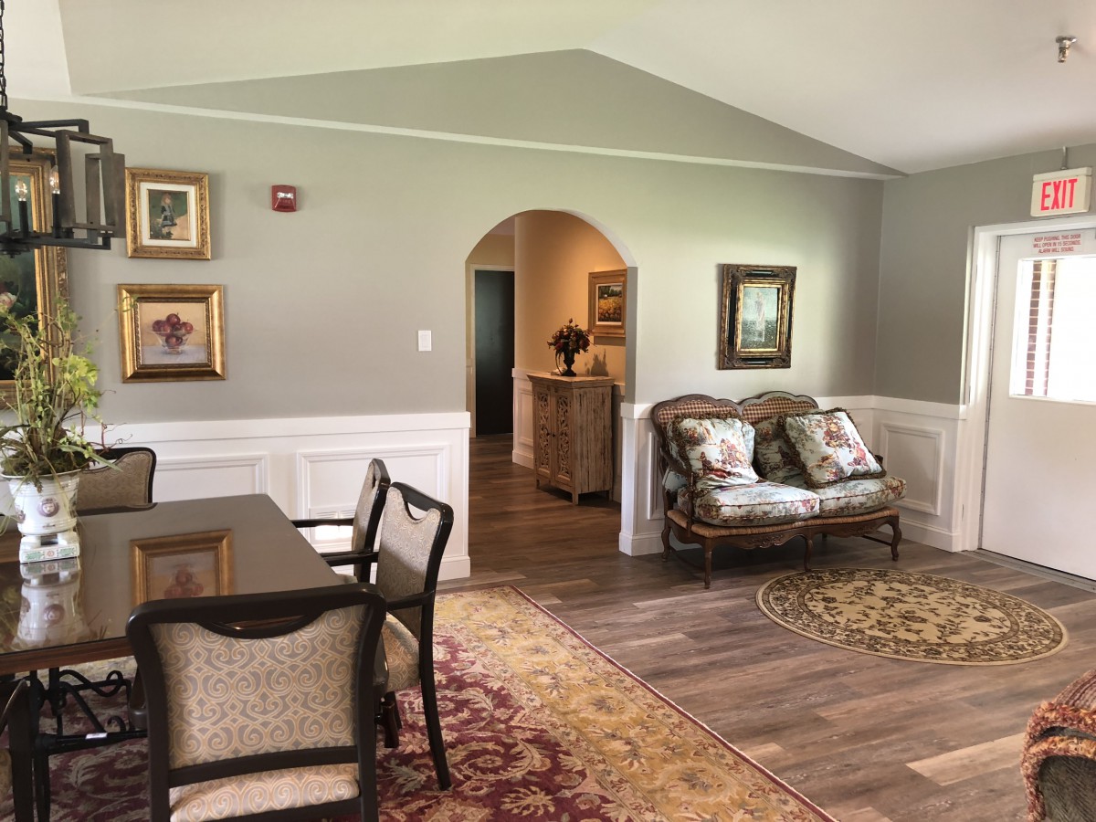 A cozy living room and dining area featuring classic furniture, decorative paintings, and warm lighting.