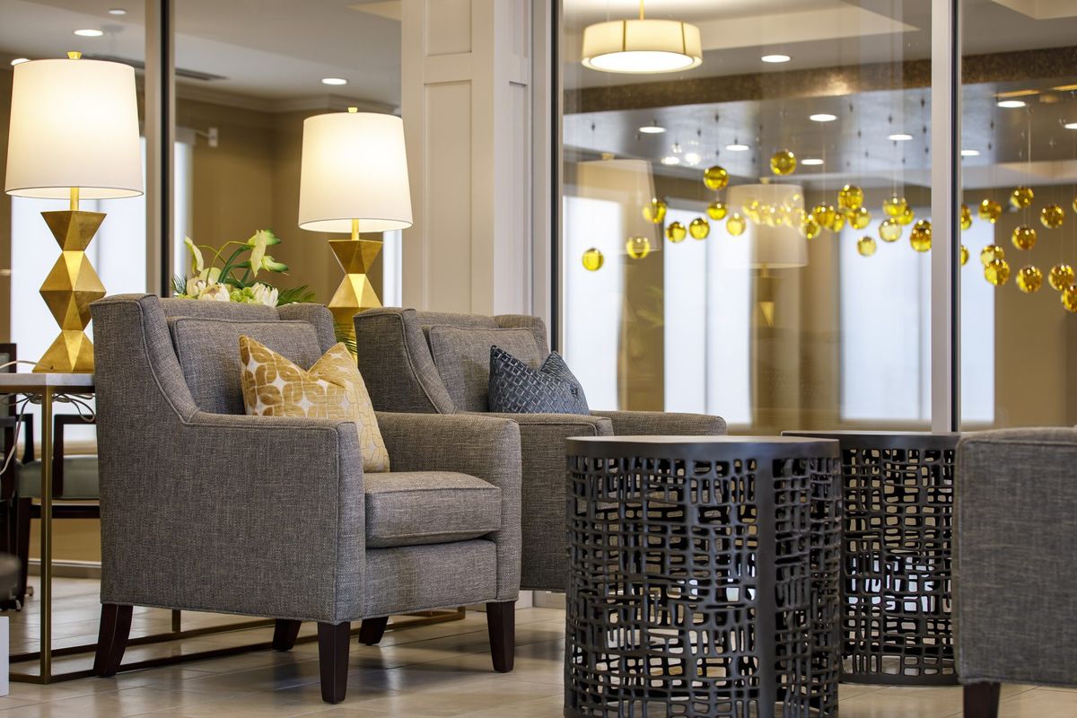 A modern living room with gray armchairs, a decorative table, and a lit lamp in the background.