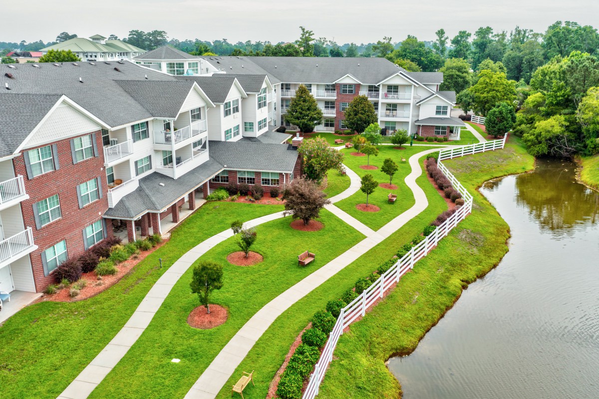 Aerial view of a well-maintained apartment complex with landscaped gardens and walking paths alongside a pond.