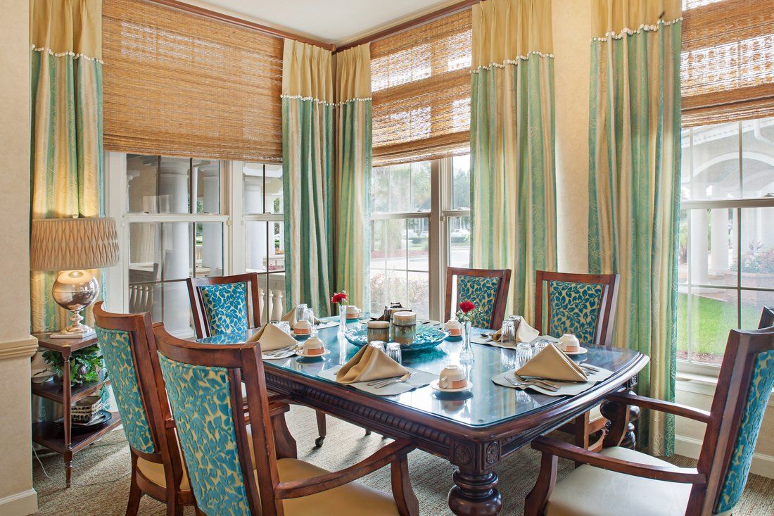 A beautifully set dining table in a well-lit room with elegant curtains and wooden chairs.