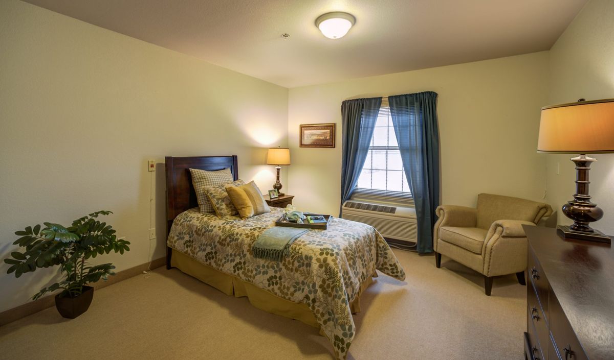 Cozy bedroom with a comfortable bed, elegant lamp, and window with blue curtains.