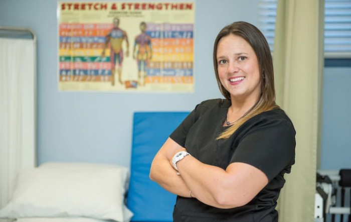 A healthcare professional standing confidently in a medical office with an exercise poster in the background.