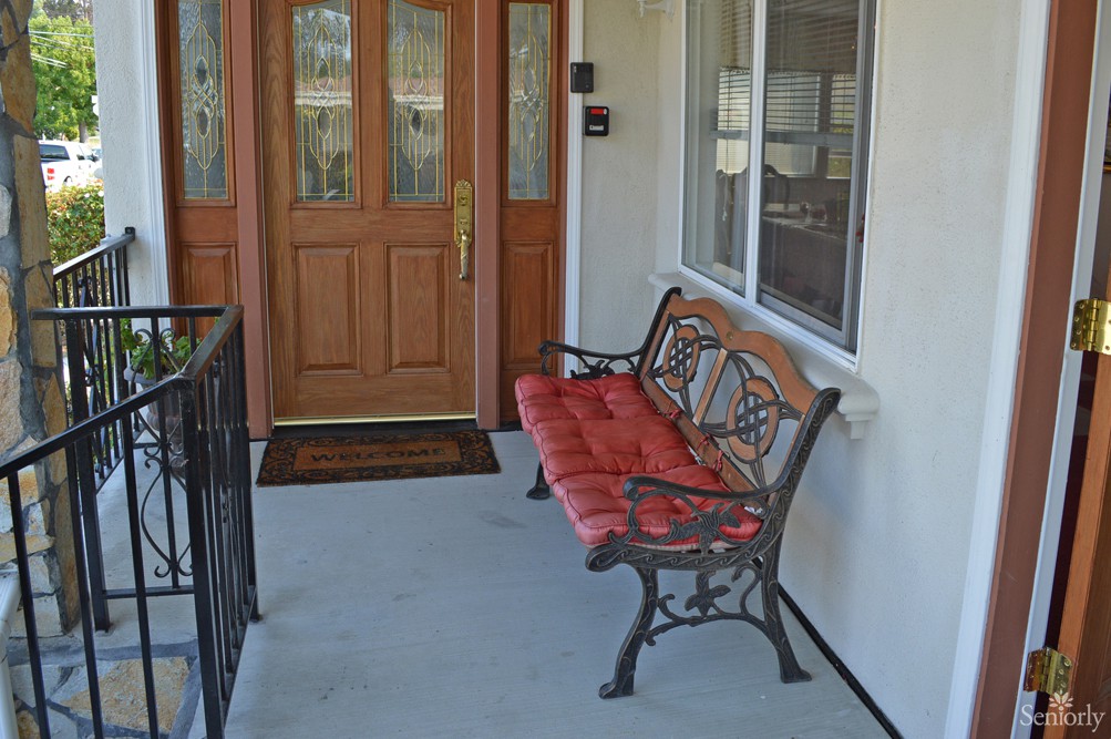 A porch with a wooden door and a bench with red cushions.