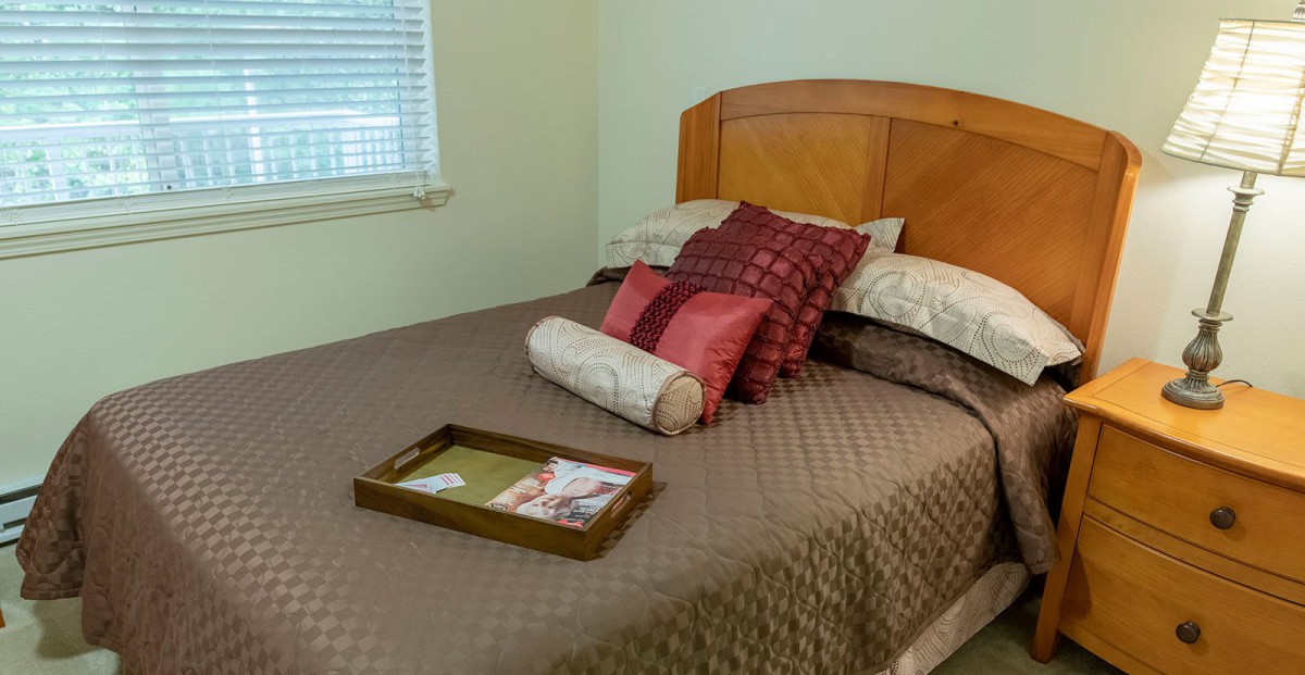 A neatly arranged bedroom with a wooden headboard, decorated with pillows and a tray on the bed.