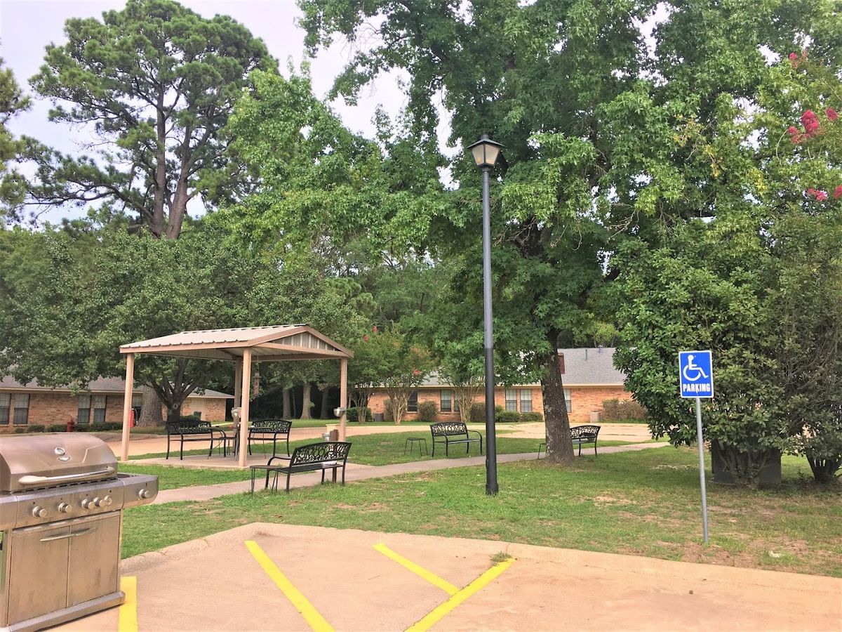 A peaceful park setting with a pavilion and benches, surrounded by trees and featuring designated handicap parking.