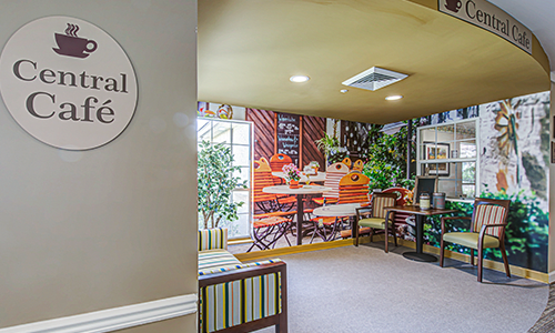 A cozy waiting area with a wall mural depicting an outdoor caf scene, complemented by comfortable seating and decorative plants.