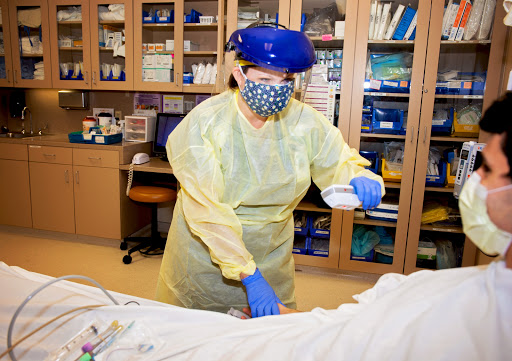 A healthcare worker in protective gear attends to a patient in a hospital setting.