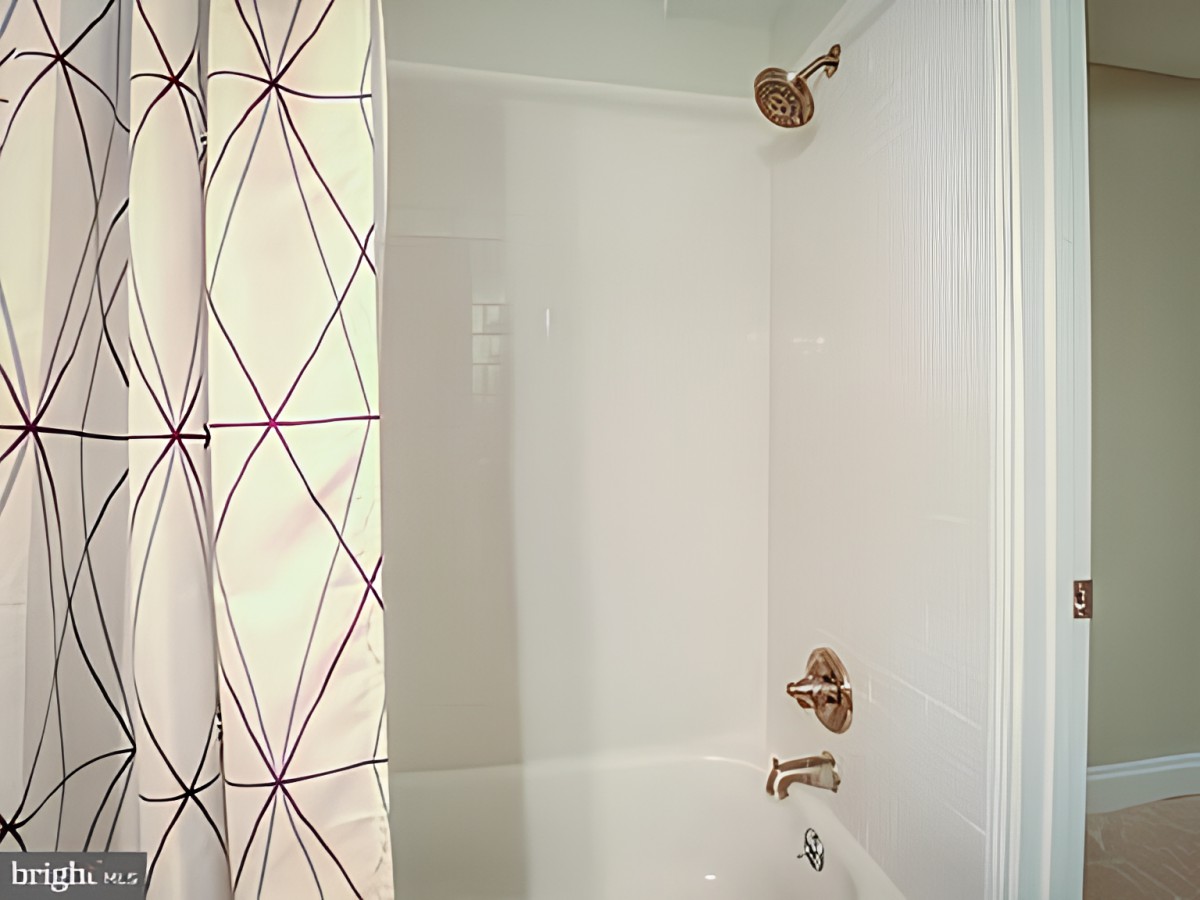 A bathroom featuring a white bathtub with a patterned shower curtain and bronze fixtures.
