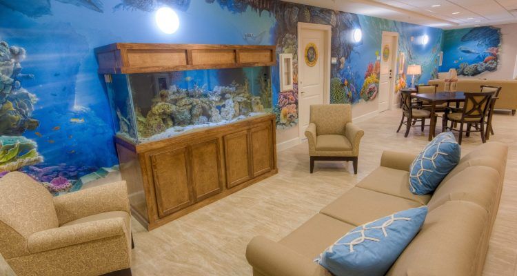 A cozy living room featuring a large aquarium, comfortable seating, and a colorful wall mural.