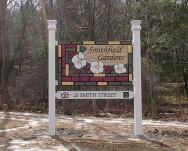 A wooden sign for a garden, located outdoors amidst trees.