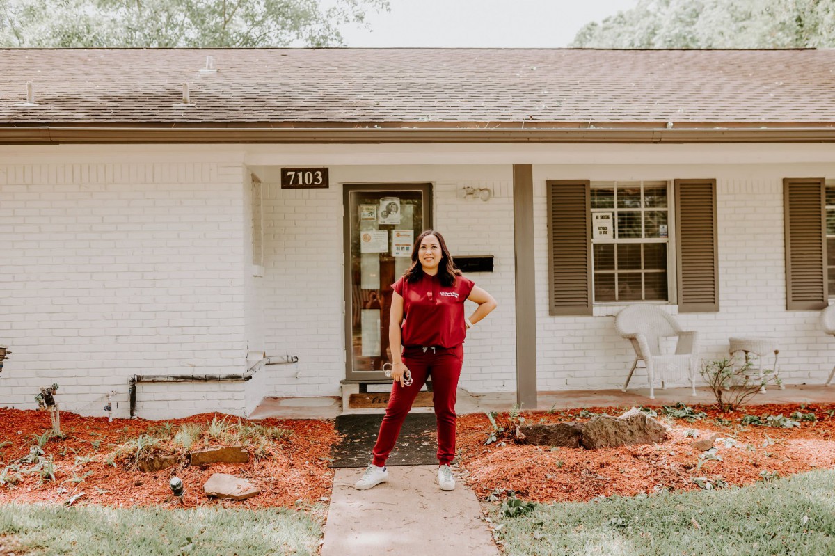 A woman standing in front of a house, posing confidently.