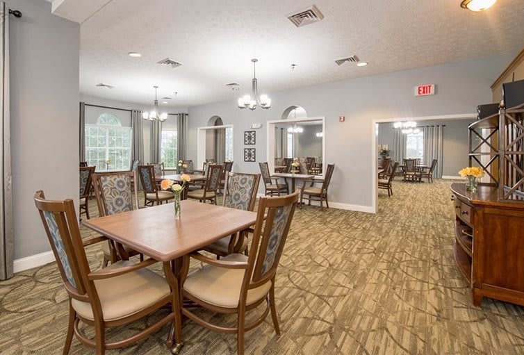 A spacious dining area with multiple tables and chairs, featuring bright lighting and a carpeted floor.