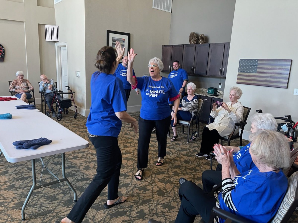 A lively community event where seniors are celebrating and sharing a high five in a cozy indoor setting.