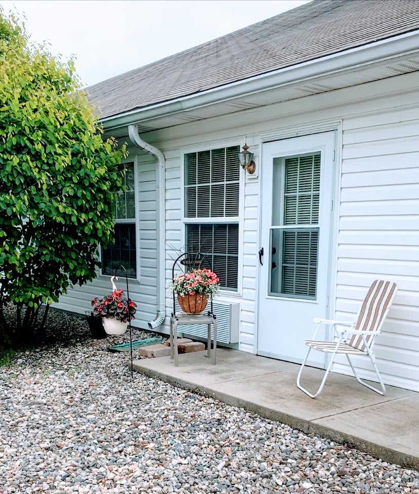 A cozy patio area with a door, windows, potted plants, and a chair.