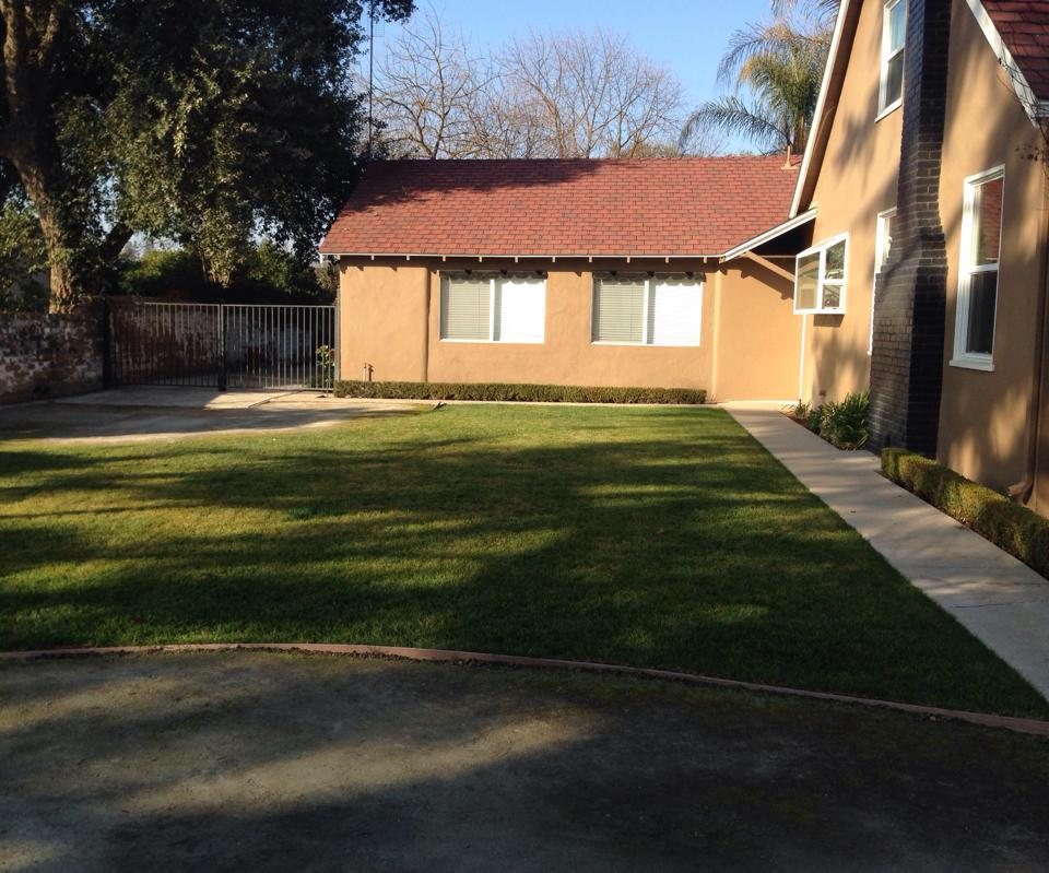 A spacious yard with a well-maintained lawn next to a brick house.