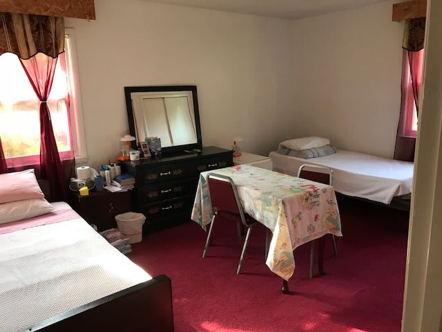 A shared bedroom with twin beds, a dresser with a mirror, and a small table with chairs on a carpeted floor.