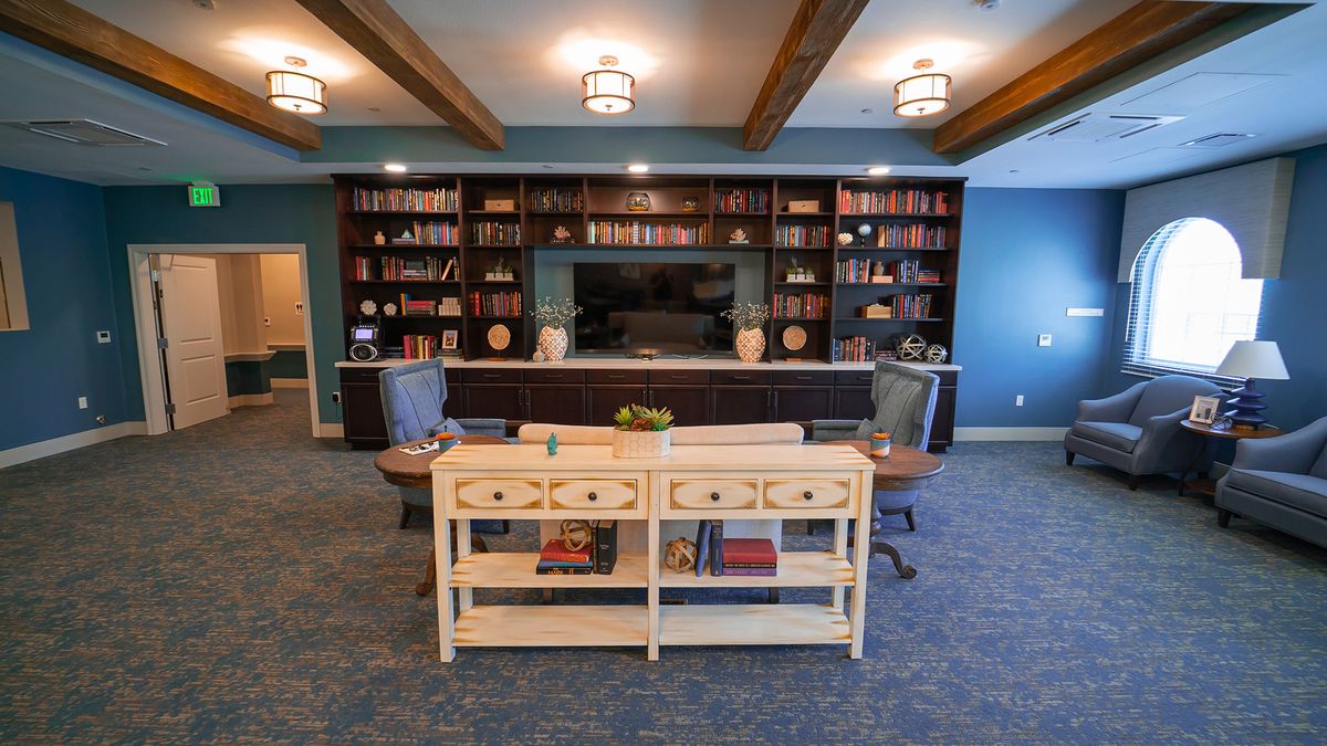 A cozy library room featuring a large bookshelf, seating area, and wooden ceiling beams.