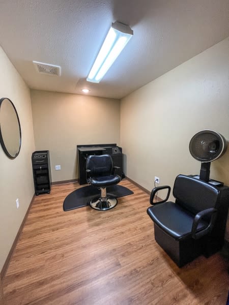 A small beauty salon room with a hairdressing chair, mirror, and dryer.