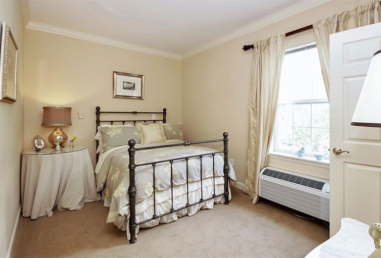 A cozy bedroom with a traditional iron bed frame, soft neutral tones, and ample natural light from a large window.