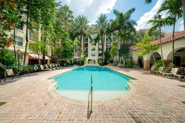 A serene outdoor swimming pool surrounded by lush palm trees and a resort building.