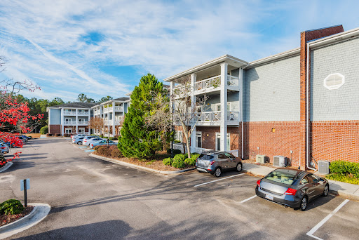 A view of a multi-story apartment complex with landscaped surroundings and a parking lot.