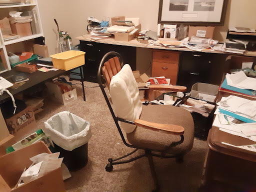 A cluttered home office filled with papers and other items, showcasing a disorganized workspace.