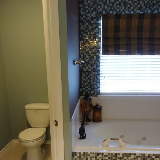 A bathroom with a bathtub and toilet, featuring a window with blinds.