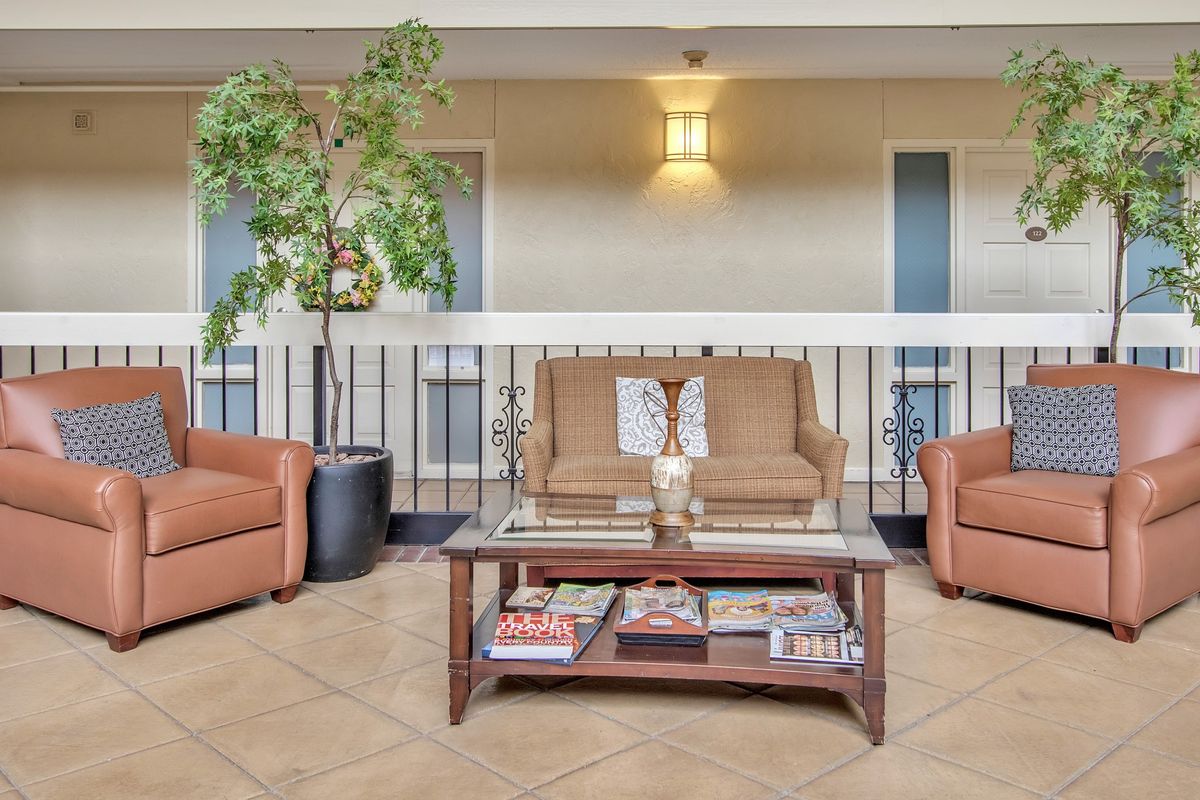 A cozy seating area featuring a sofa and two armchairs with a glass-top coffee table adorned with magazines and decorative pieces, complemented by indoor plants.