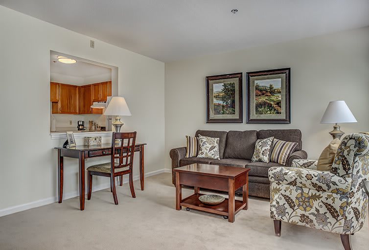 A cozy living room with a comfortable sofa and coffee table, featuring framed art and an adjacent dining area.