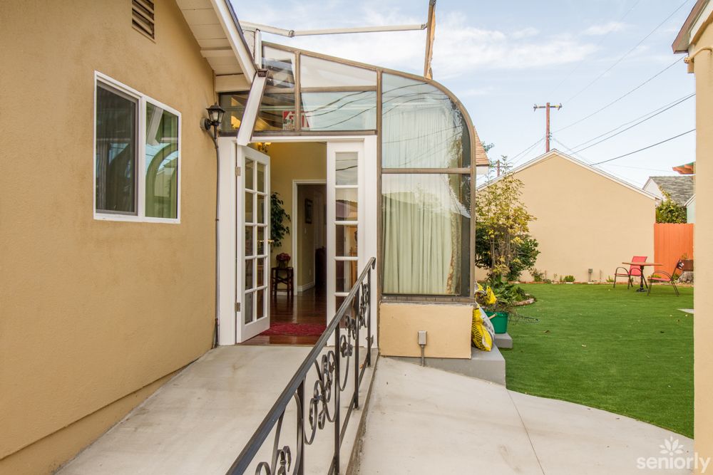 A house with a patio, featuring a glass-enclosed sunroom and garden area.