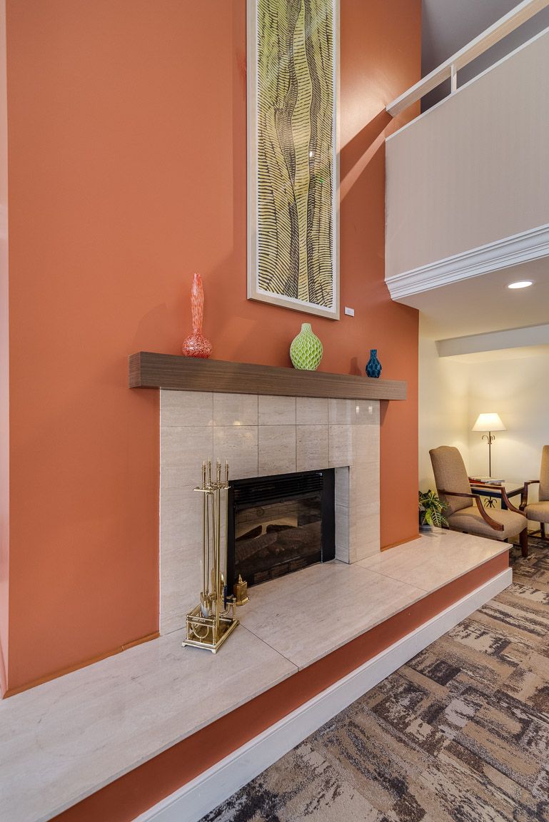 A cozy living room with an orange accent wall featuring a fireplace, decorative vases, and artwork.