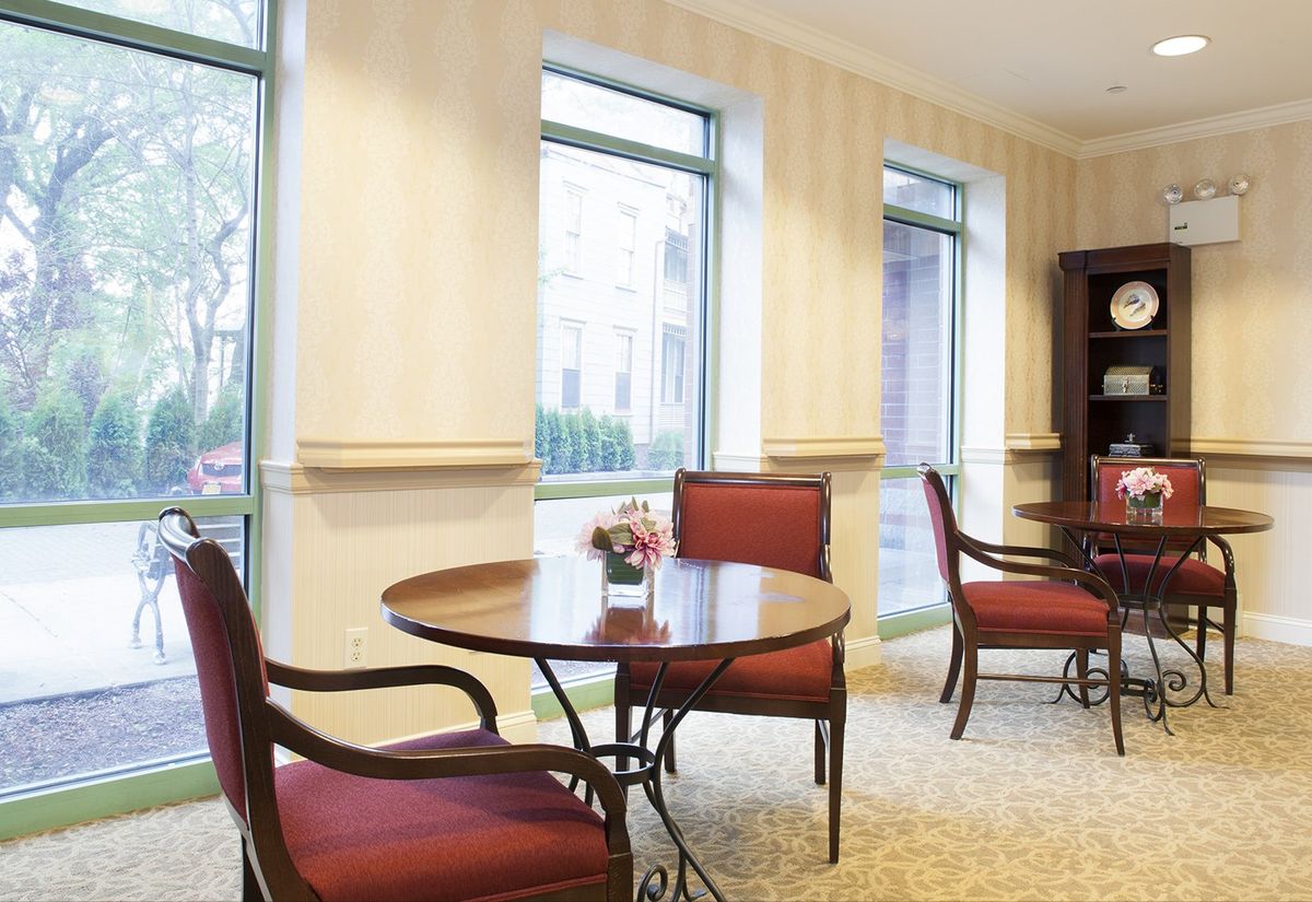 A well-lit room featuring a round table with red upholstered chairs and large windows.