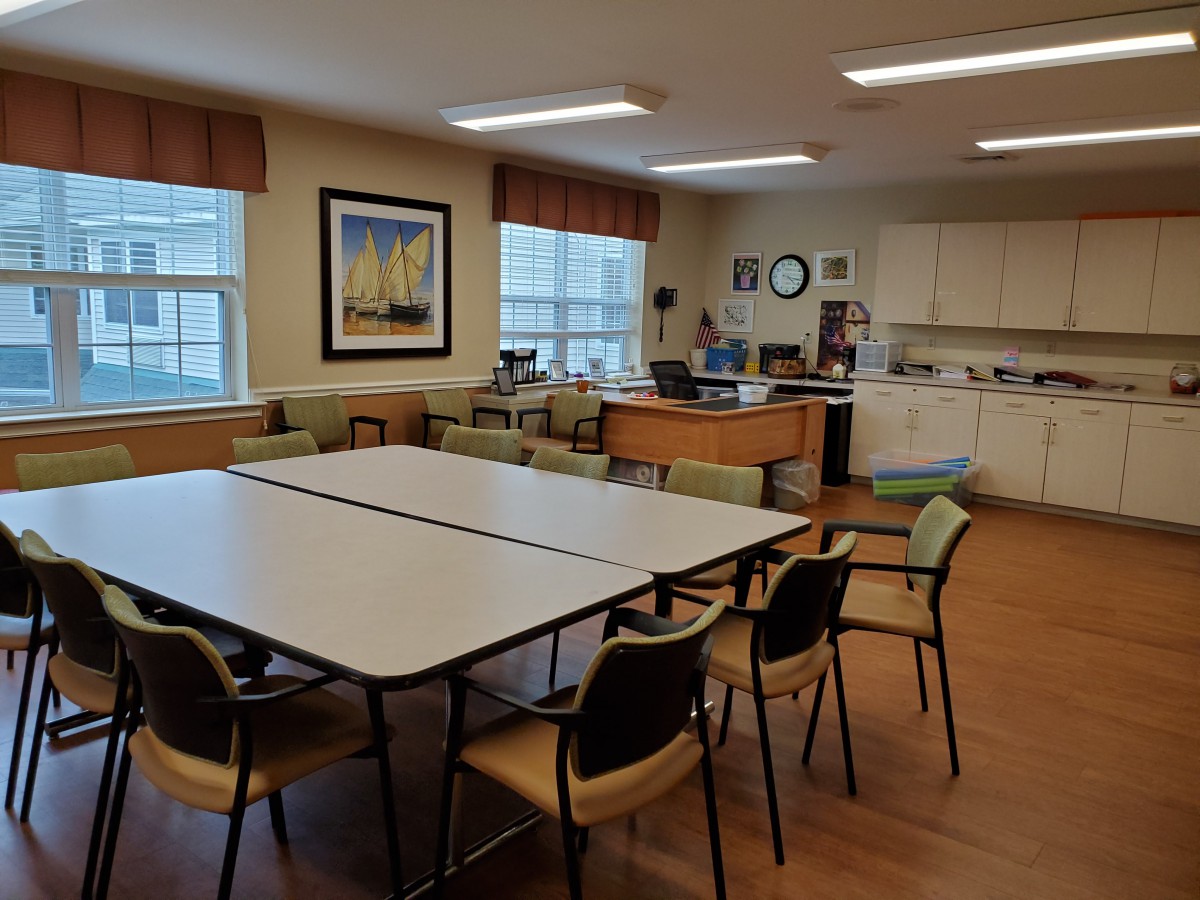 A well-organized meeting room with tables and chairs, featuring a small kitchenette and framed artwork.