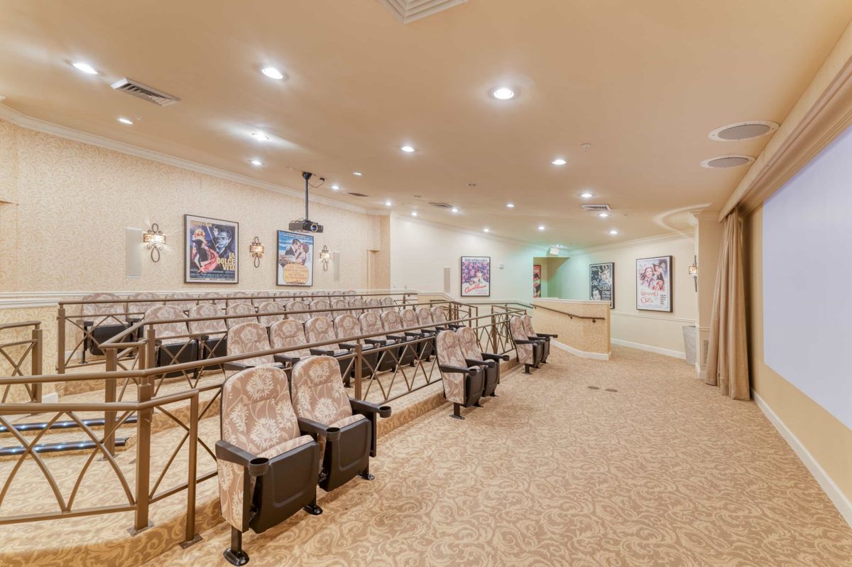 An indoor theater with rows of chairs and a projection screen, featuring a carpeted floor and ceiling lights.