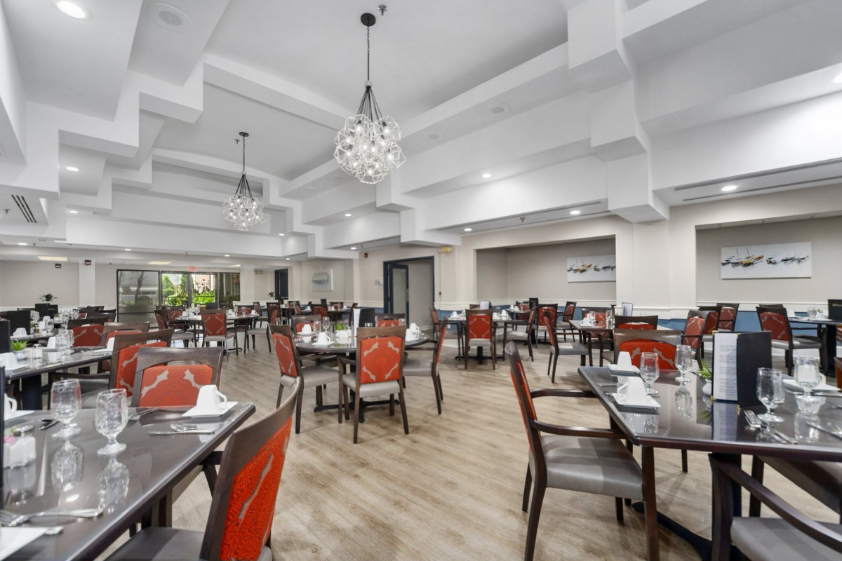 A spacious and elegant restaurant dining area with red chairs and wooden tables under modern chandeliers.