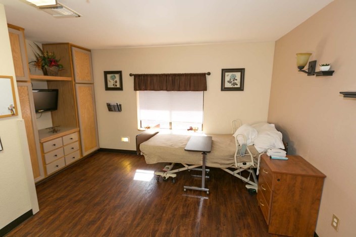 A well-lit hospital room with a single bed, wooden flooring, and minimalistic decor.