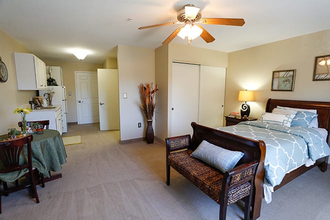A cozy and well-furnished bedroom featuring a ceiling fan, a bed with bedside lamps, and a decorative bench.