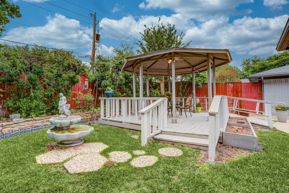 A serene garden setting featuring a white gazebo with surrounding lush greenery and a decorative fountain.
