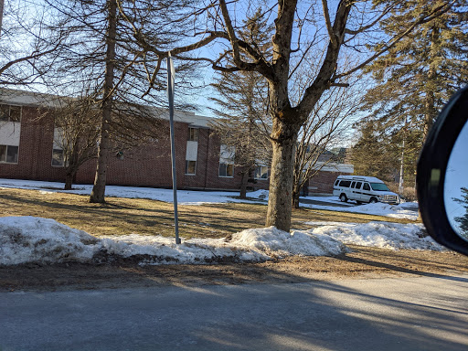 A serene winter scene featuring a building surrounded by snow and bare trees, with a van parked nearby.